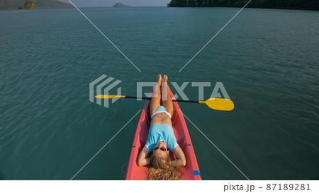 Pretty slim woman in elegant swimsuit lies in pink plastic kayak drifting on azure ocean at exotic resort upper view. 87189281