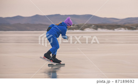 The girl train on ice speed skating. The child skates in the winter in blue sportswear suit, sport glasses. Children speed skating sport. The girl train on ice speed skating. The child skates in the winter in blue sportswear suit, sport glasses. Children speed skating sport. 87189692