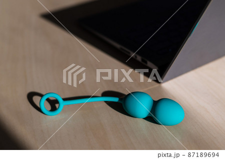 Blue silicone vaginal kegel balls on a table next to a laptop. Sex toy for building is synchronized with a computer. Intimate muscle trainer for women health. 87189694