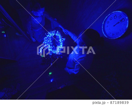 The family fast and fanny decorates the Christmas tree. Top view. Time on the clock is 23.45 on wall. Happy dad, mom, daughter are run around tree. 87189839