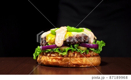 Craft burger is cooking on black background. Consist: sauce salsa, lettuce, red onion, pickle, cheese, chilli green pepper, bun, marbled meat beef. Craft burger is cooking on black background. Consist: sauce salsa, lettuce, red onion, pickle, cheese, chilli green pepper, bun, marbled meat beef. 87189968