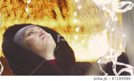 Pretty woman walking along the black fur coat. Outdoor. Girl walks on a winter night among the street lights of the city. Snow park with garlands. 87189986