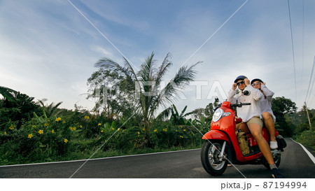 Love couple on red motorbike in white clothes to go on forest road trail trip. Two caucasian tourist woman man drive on scooter. Motorcycle rent. 87194994