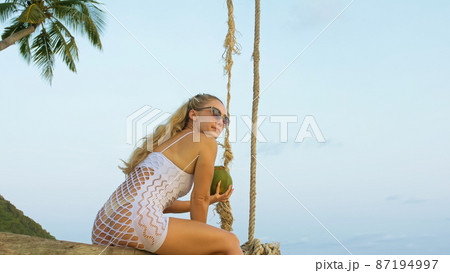Attractive woman is swinging on a swing. Sexy hot erotic bad girl posing on the beach against the backdrop of the sea. Concept natural beauty body, femininity and sexuality, debauchery and courage. 87194997