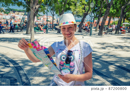 Young beautiful woman traveler with white hat looking at camera, smiling and searching direction on location map in sunny summer day 87200800