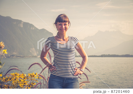 Young beautiful girl with striped shirt and jeans posing and smile on embankment of Lake Leman Geneva 87201460