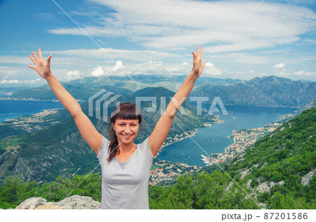 Young beautiful girl traveler with grey t-shirt raise hands and smile on top of mountain Young beautiful girl traveler with grey t-shirt raise hands and smile on top of mountain 87201586