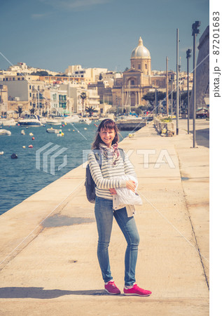 Young girl traveler stay and posing on embankment of Kalkara Creek of Malta's Grand Harbour 87201683