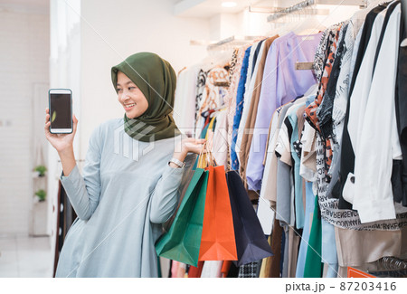 beautiful girl wearing a hijab holding a smartphone and showing to camera 87203416