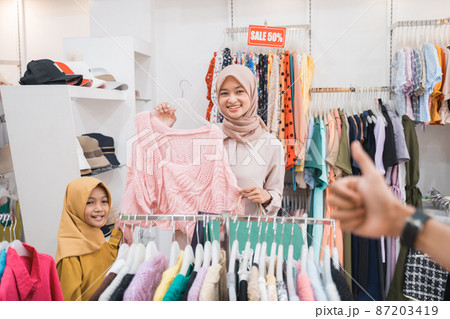 muslim mother choosing shirt with daughter during shopping at fashion shop 87203419