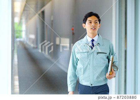 オフィスの廊下を歩く作業服を着た若いエンジニア オフィスの廊下を歩く作業服を着た若いエンジニア 87203880