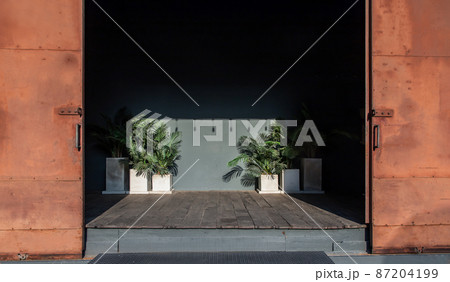 Old warehouse with steel orange door and entrance with plants in white pots. Old warehouse with steel orange door and entrance with plants in white pots. 87204199