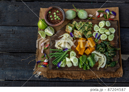 Thai Traditional Local Food : Spicy Shrimp Paste Dip or Fried shrimp paste sauce (Nam Prik Kapi) with blanched vegetables and cha-om omelets on wooden backgroud. 87204587
