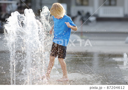 Little boy plays in the square between the water jets in the dry fountain at sunny summer day. Active leisure for kids in the city. 87204612