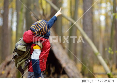 Little boy scout during hiking in autumn forest. Behind the child is teepee hut. Adventure, scouting and hiking tourism for kids. 87204614