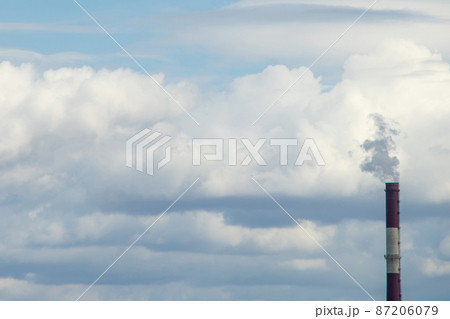 Smoke from a red-and-white pipe of a thermal power plant against a background of white clouds and blue sky Smoke from a red-and-white pipe of a thermal power plant against a background of white clouds and blue sky 87206079