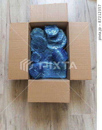 Glassware wrapped with blue wrapping nylon at the bottom of a cardboard box. Glassware wrapped in a box. Top view. Flat lay. Copy space 87212357