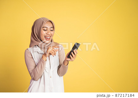 muslim woman laughing at her smartphone isolated on yellow muslim woman laughing at her smartphone isolated on yellow 87217184