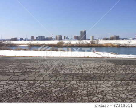 ひび割れた江戸川土手の専用道路から見る残雪の河川敷と対岸風景 ひび割れた江戸川土手の専用道路から見る残雪の河川敷と対岸風景 87218611