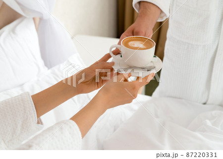 Closeup of a man bringing coffee to his girlfriend lying in bed 87220331