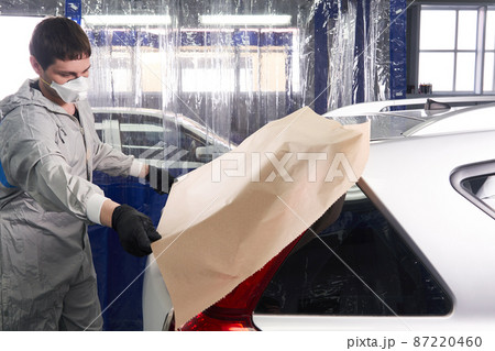 Mechanic covering car with paper before painting in auto repair service Mechanic covering car with paper before painting in auto repair service 87220460