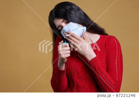 Young girl wearing medical protective mask lights up, holding a cigarette in her mouth through the mask 87221246