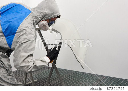 Mechanic painting bumper of a car with sprayer in painting booth in repair auto service 87221745