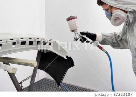Mechanic painting bumper of a car with sprayer in painting booth in repair auto service 87223107
