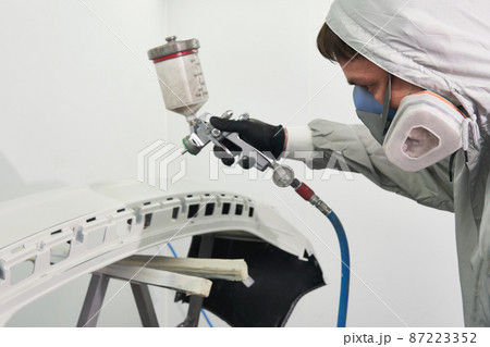 Mechanic painting bumper of a car with sprayer in painting booth in repair auto service Mechanic painting bumper of a car with sprayer in painting booth in repair auto service 87223352