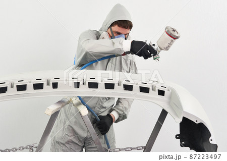 Mechanic painting bumper of a car with sprayer in painting booth in repair auto service Mechanic painting bumper of a car with sprayer in painting booth in repair auto service 87223497