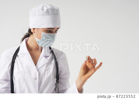 Doctor wearing face mask looking at measurement on medical thermometer over white background  87223552