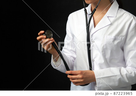 Cropped view of young female doctor holding stethoscope hanging on her neck, studio shot over black background with copy space 87223965