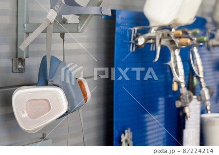 Professional respirator in auto repair shop with spray guns on background 87224214