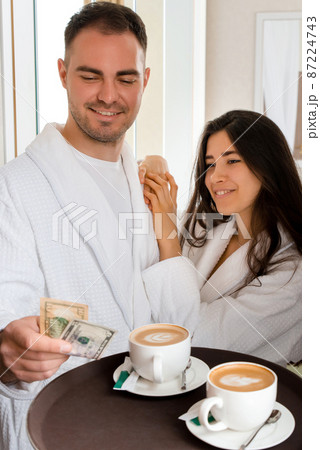 Room service delivering coffee to a hotel room for married couple wearing bathrobe who is giving dollar tips 87224743