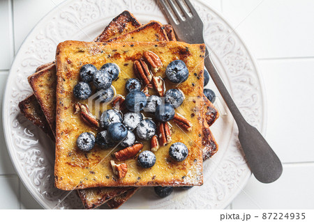 French toast with blueberries, pecan and maple syrup for breakfast on white plate. 87224935
