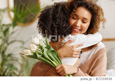 Young ethnic woman mother with flower bouquet embracing son while getting congratulations on Mother's day 87234030