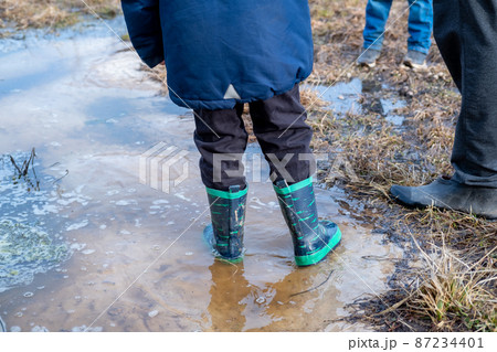 A child in boots walks and jumps in a muddy puddle after rain. Mud after melting snow. 87234401