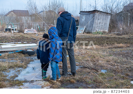 Dad and two children look at the destroyed area. Village after the flood. Refugees in a destroyed village. 87234403