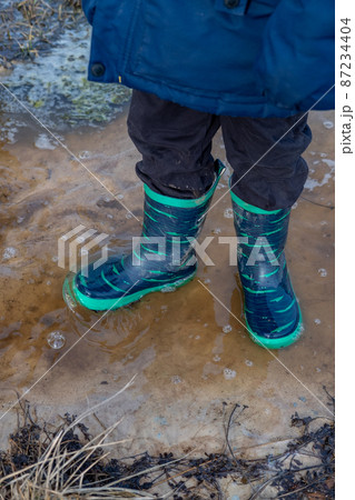A child in boots walks and jumps in a muddy puddle after rain. Mud after melting snow. A child in boots walks and jumps in a muddy puddle after rain. Mud after melting snow. 87234404