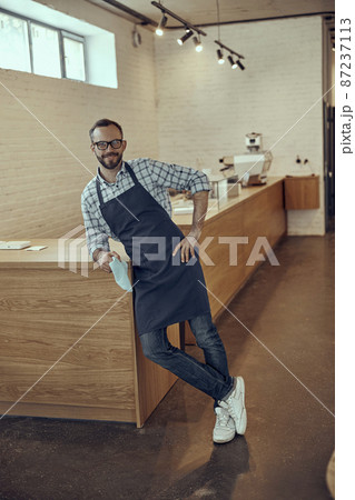 Cheerful male bartender leaning on counter in cafe Cheerful male bartender leaning on counter in cafe 87237113