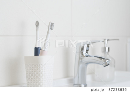 New modern ultrasonic toothbrushes in a glass on the bathroom sink. Jaw model and dental care supplies. Oral hygiene, dental and gum health, healthy teeth. Dental products 87238636