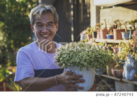 asian man holding house plant pot and toothy smiling with happiness 87240743
