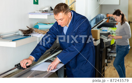 Printing worker cuts paper on a cutter machine Printing worker cuts paper on a cutter machine 87243579