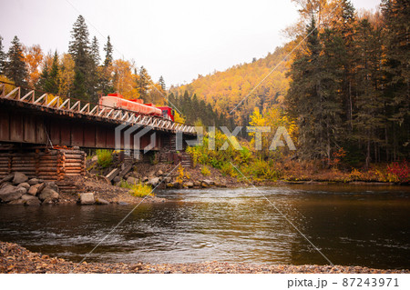 Red fuel truck at wooden bridge over mountain river in autumn 87243971