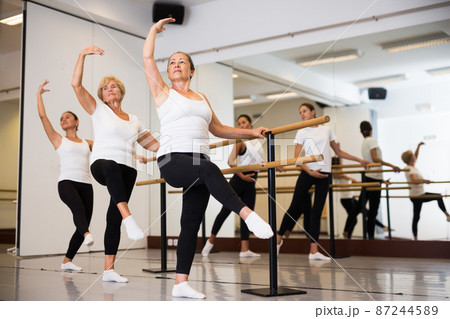 Group of people doing exercises using barre in gym with focus to fit athletic toned woman in foreground in health Group of people doing exercises using barre in gym with focus to fit athletic toned woman in foreground in health 87244589