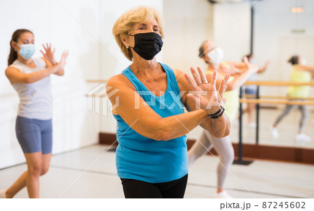 Active mature woman in a protective mask practices energetic swing in the studio Active mature woman in a protective mask practices energetic swing in the studio 87245602