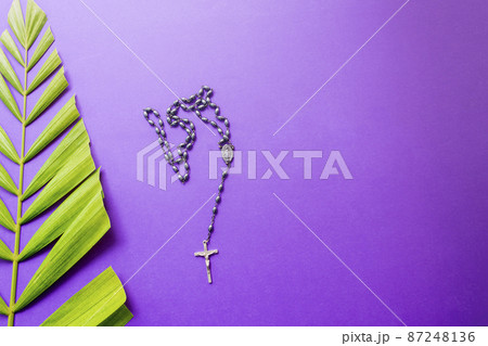 Cross and palm leaves on purple background. Lent season concept. Cross and palm leaves on purple background. Lent season concept. 87248136