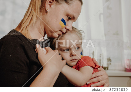 Ukrainian young mother with daughter with flag on the face with fear suffering and praying peace during war conflict between Russia and Ukraine, invasion of Russia in Ukraine 87252839