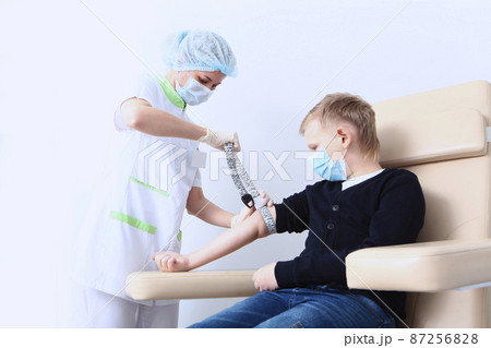 A boy in a protective mask is donating blood in a medical laboratory. A general blood test. Blood from the finger.A nurse and a child. The concept of healthcare.Medical laboratory. 87256828