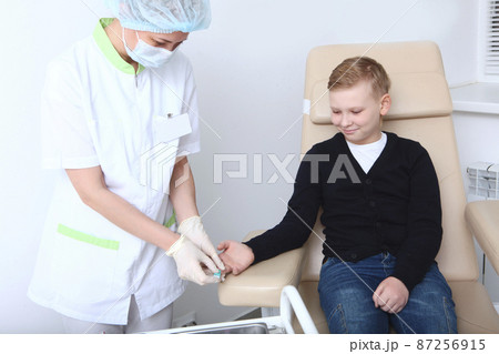 The boy is donating blood in a medical laboratory. A general blood test. Blood from the finger.A nurse and a child. The concept of healthcare. 87256915